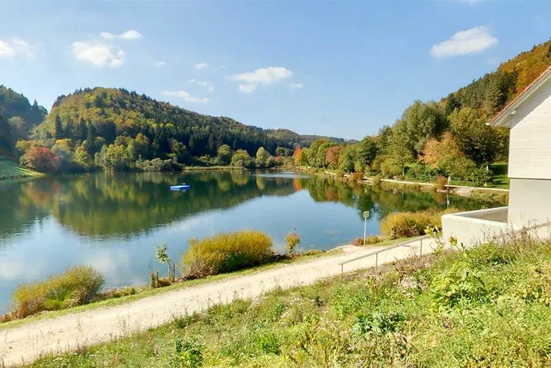 Der Stausee Oberdigisheim mit Uferweg, Wiese und bewaldeten Hängen im Herbst