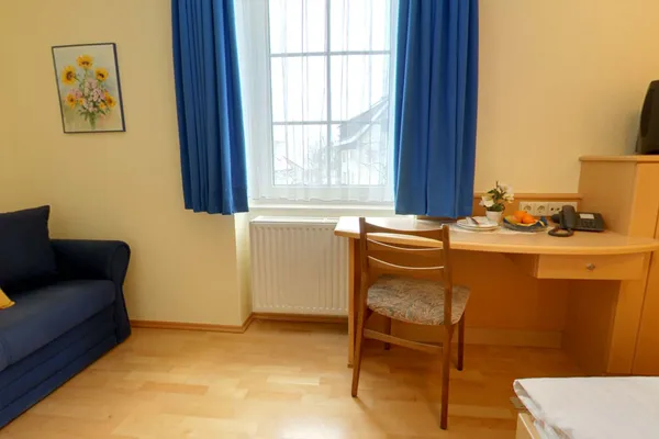 Zimmer mit Schreibtisch, Sofa und blauen Vorhängen