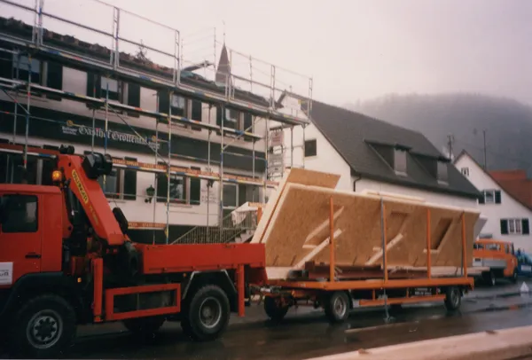 Ein Lastwagen mit Kran bringt ein fertiges Wandelement aus Holz
