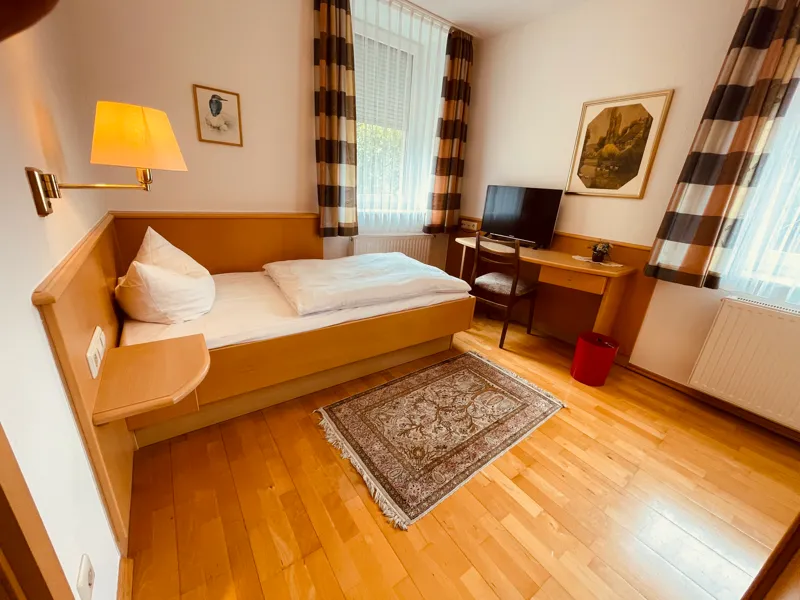 Einzelzimmer mit Bett, Schreibtisch, Fernseher und Leselampe