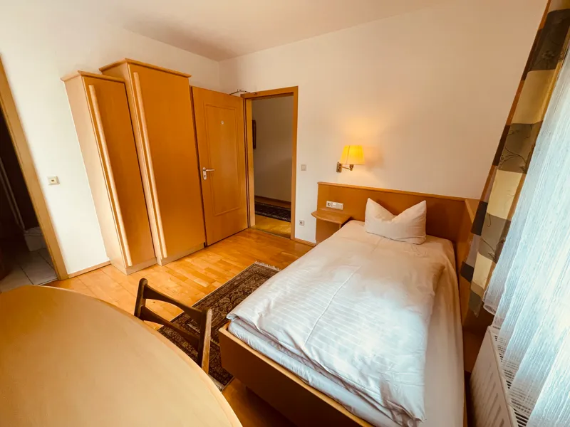 Einzelzimmer mit Bett, Kleiderschrank und Schreibtisch